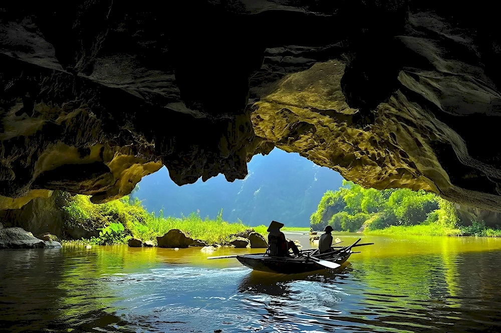 Small boats glide on the emerald-green river, passing through magnificent caves